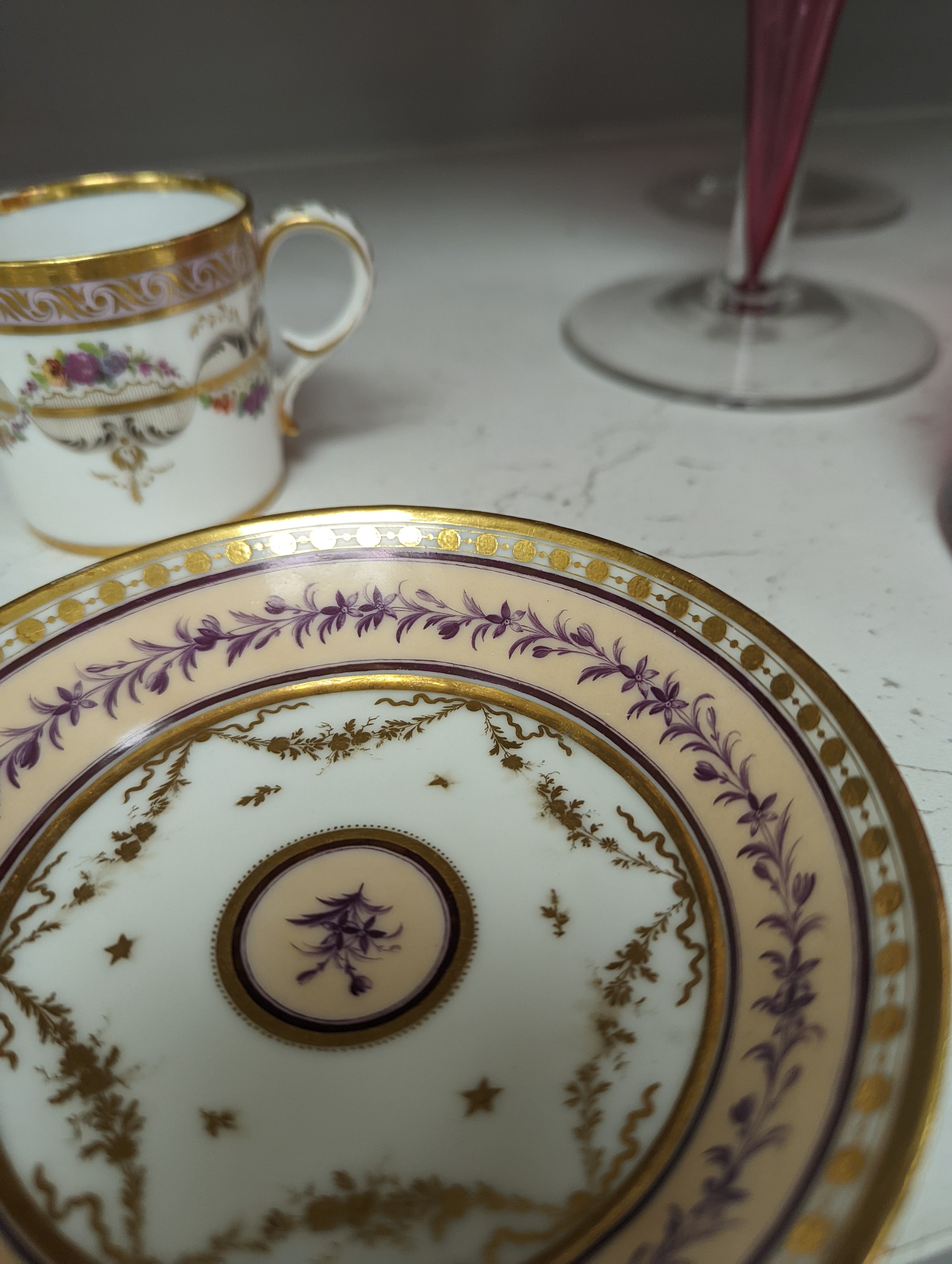 A Duc d'Angouleme coffee can and saucer painted with a puce chain of leaves on a salmon coloured ground and another painted with a flower chain, black feather and a gilt line, latter with stencilled red mark 'Manuf de M